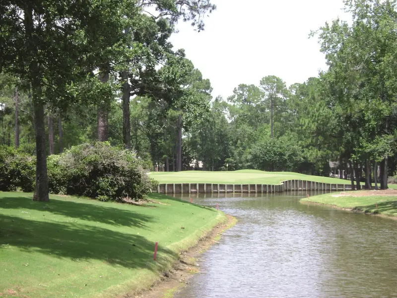 A green set behind a bulkheaded lake, framed by pines and oaks