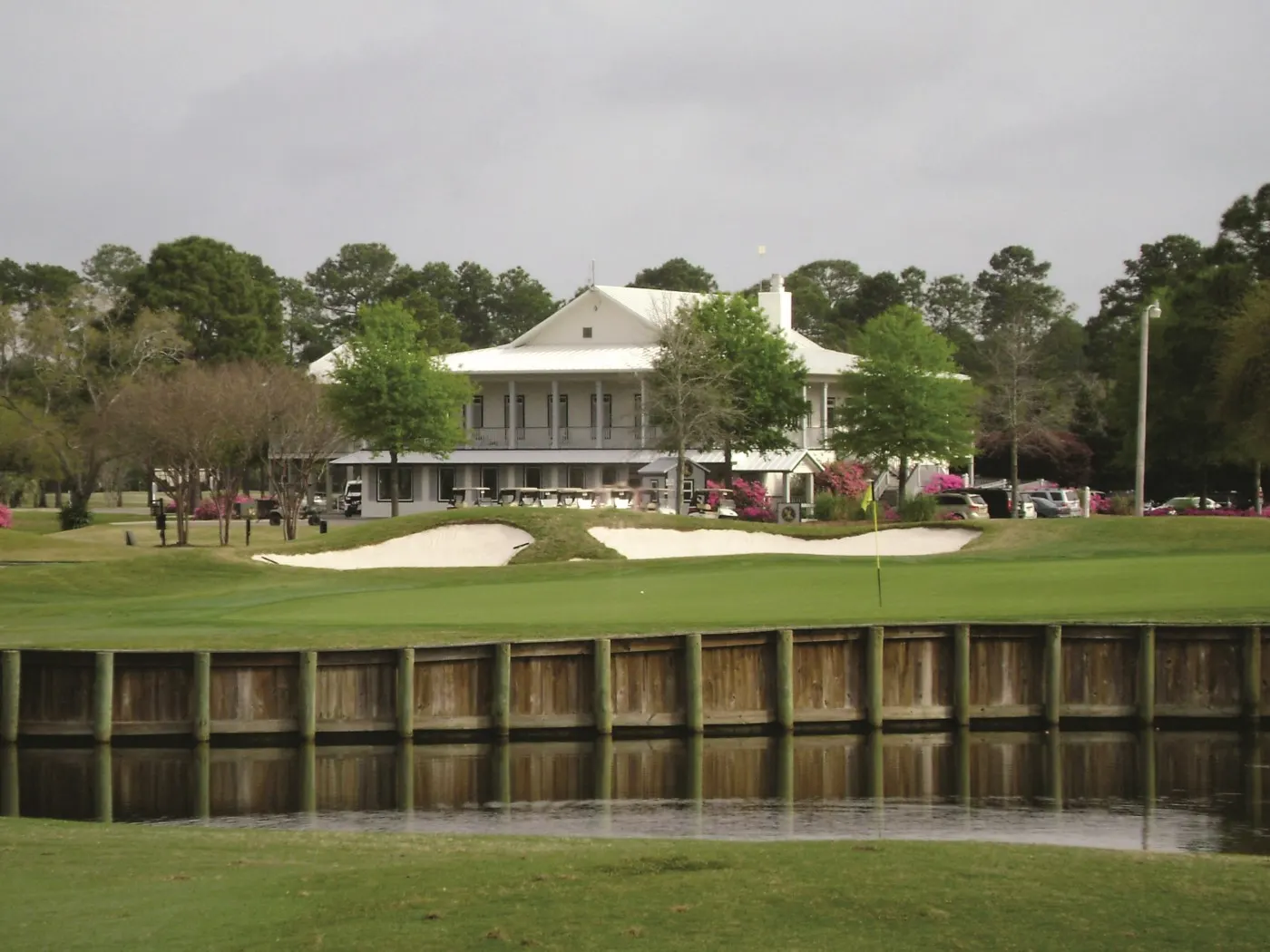 Green with a yellow flag behind a bulkheaded lake, with the clubhouse beyond