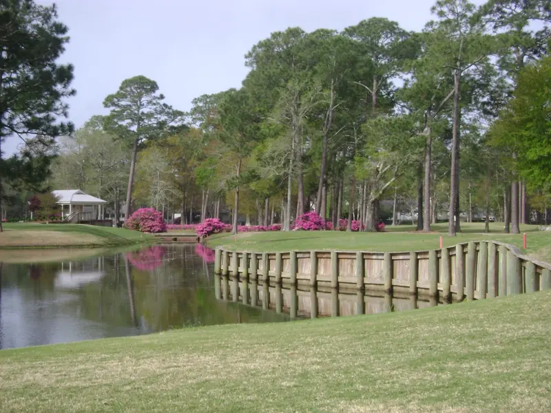 A bulkheaded lake reflecting pines and azaleas in bloom, with a small pavilion on the far bank