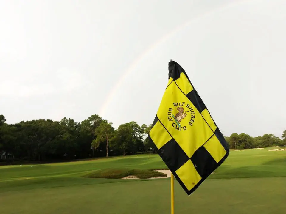 Yellow and black checkered Gulf Shores Golf Club pin flag on a green, with a rainbow behind it