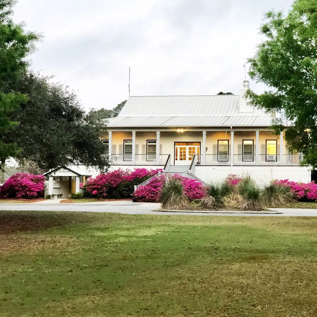 The clubhouse porch lit at dusk above a bank of pink azaleas