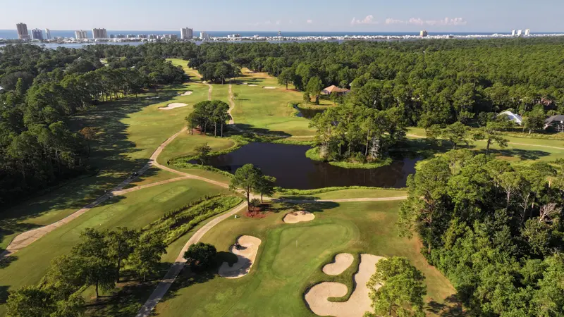 Aerial view over the fairways to a lake, with the Gulf Shores skyline on the horizon