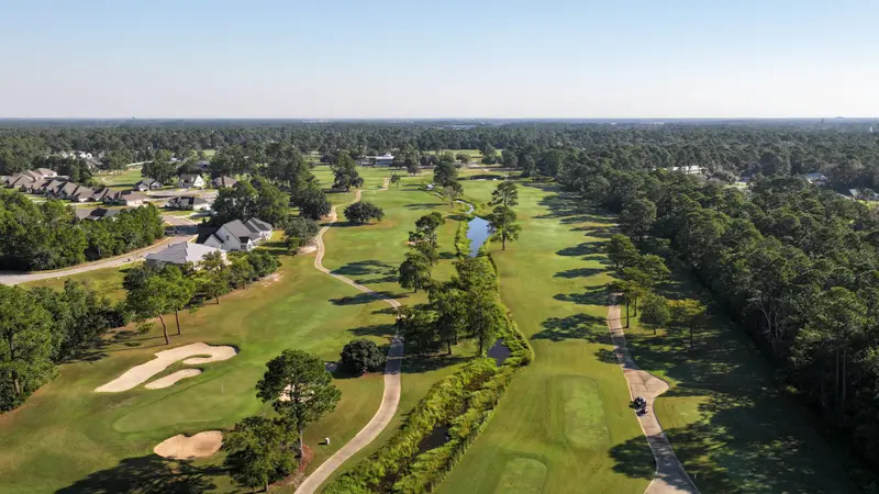 Aerial view of a fairway with homes along one side and a creek winding through the rough