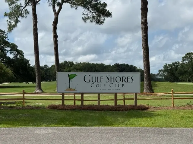 The Gulf Shores Golf Club entrance sign on a split-rail fence beside the road