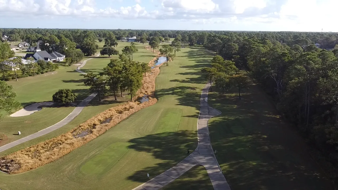 Aerial view of a long fairway at Gulf Shores Golf Club with cart paths running either side of a reed-lined creek