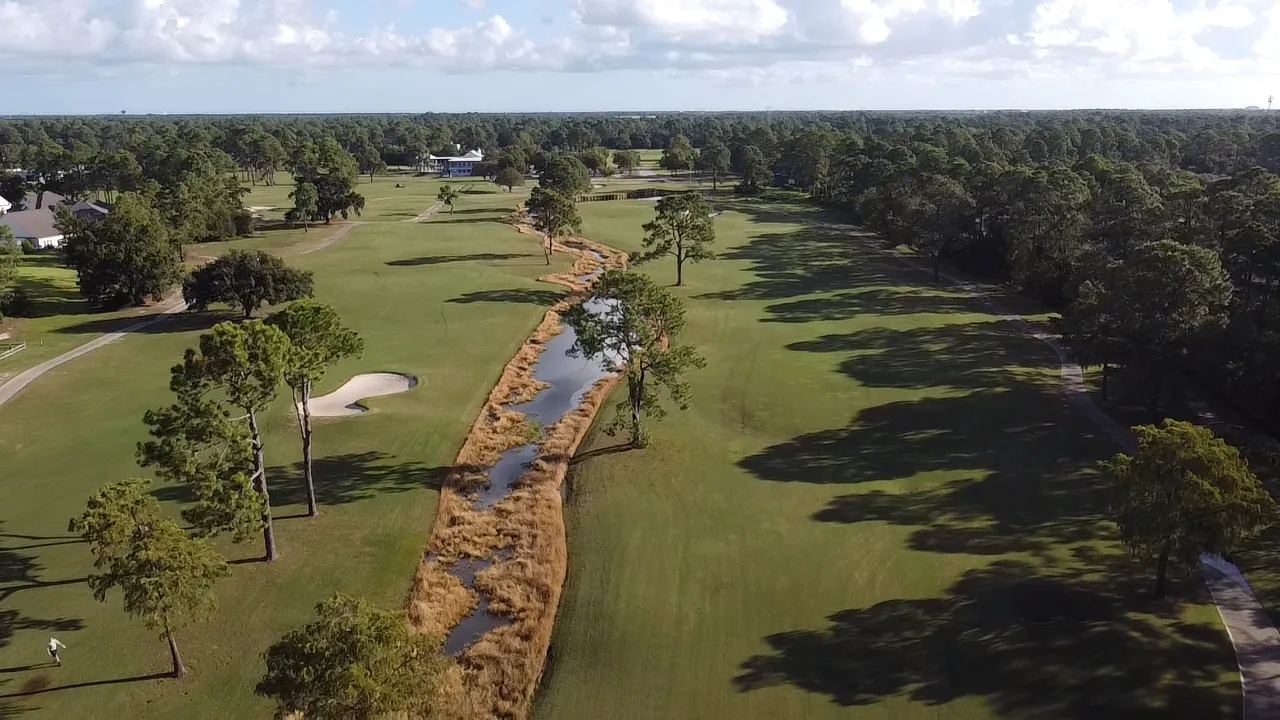 Aerial view of a reed-lined creek running between pine-dotted fairways and a bunker at Gulf Shores Golf Club