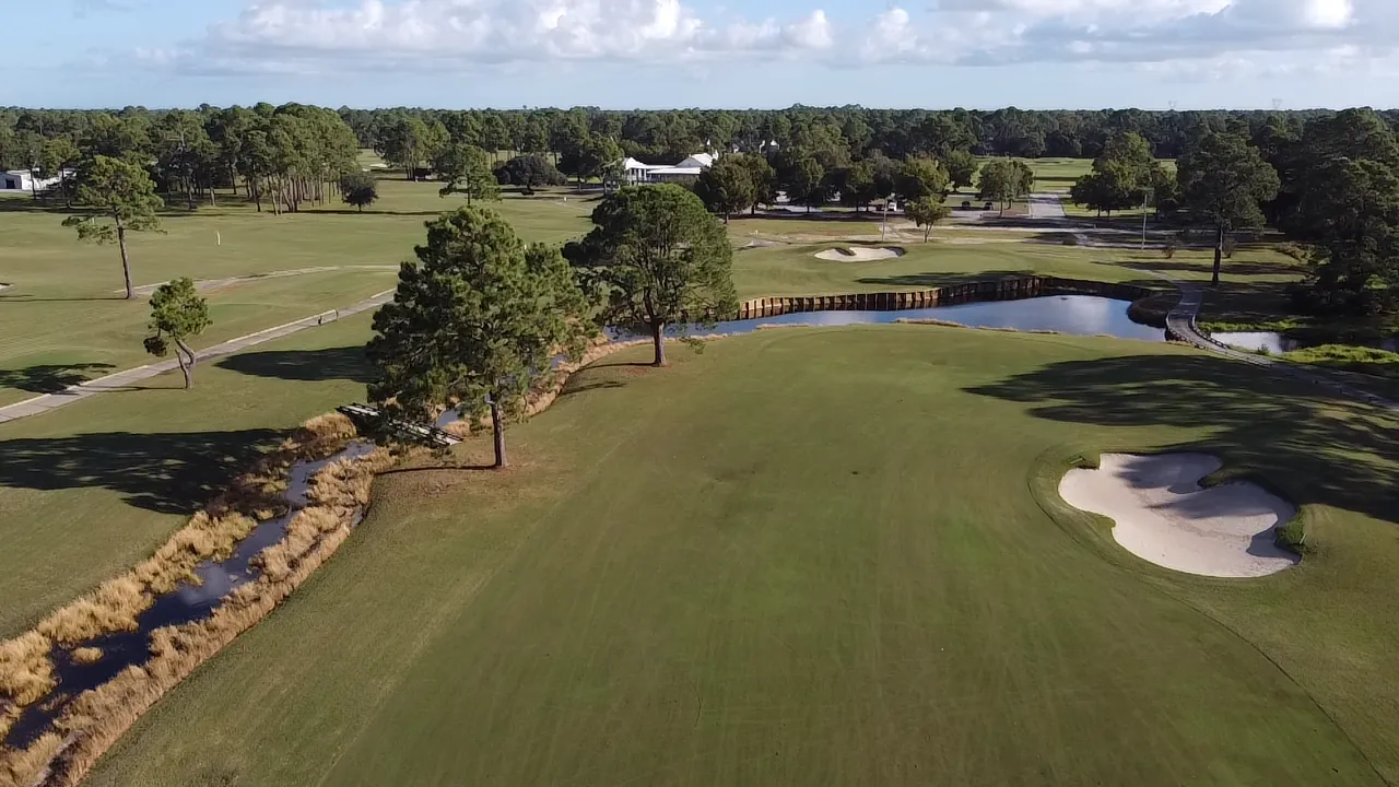 Aerial view of a fairway leading to a bunkered green and a bulkheaded pond at Gulf Shores Golf Club