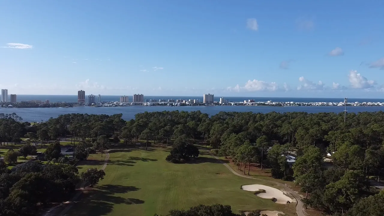Aerial view over the pines and fairways of Gulf Shores Golf Club toward the bay and the Gulf Shores skyline