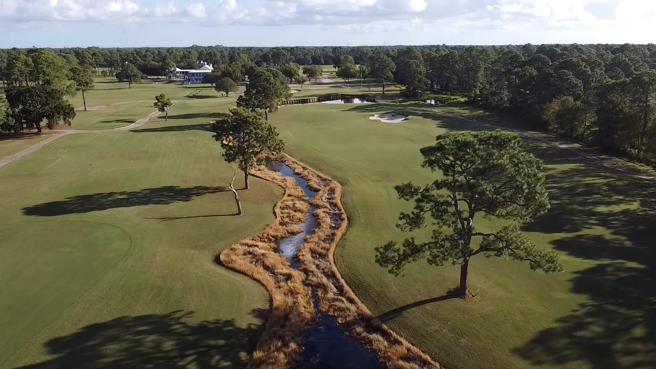 Aerial view of a creek winding through the fairway toward a bunkered green at Gulf Shores Golf Club