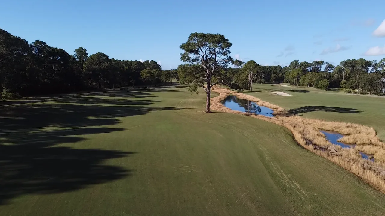 Long late-day shadows across a fairway beside a reed-lined creek at Gulf Shores Golf Club