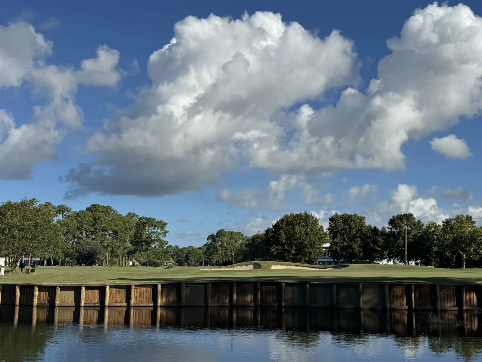 A green above a timber-bulkheaded pond under tall summer clouds at Gulf Shores Golf Club
