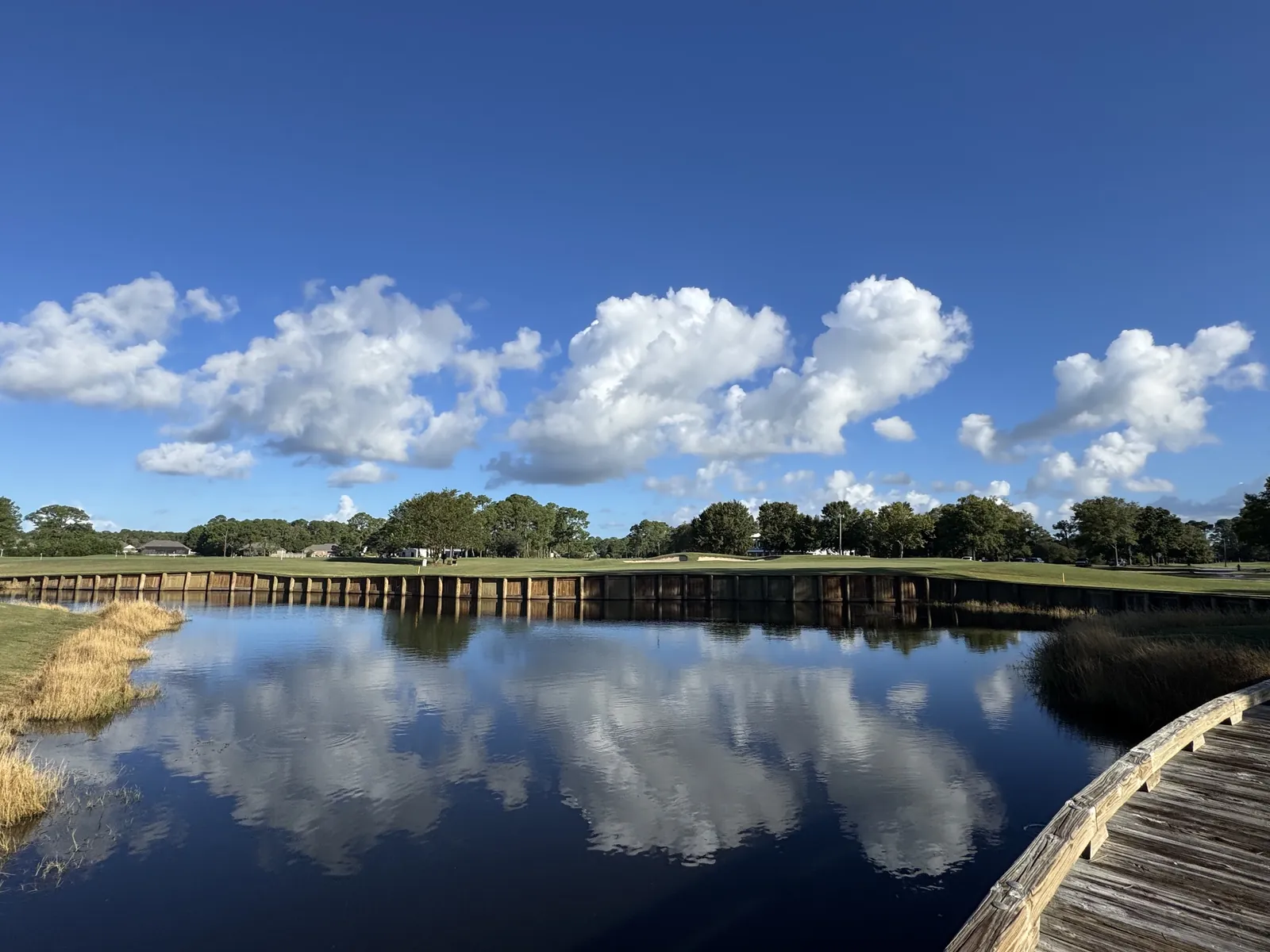 Clouds reflected in a calm lake beside a wooden boardwalk at Gulf Shores Golf Club