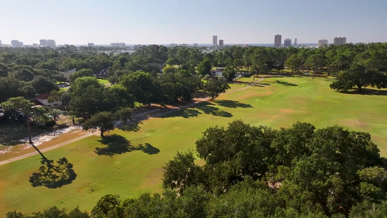 Aerial view of tree-lined fairways at Gulf Shores Golf Club with the Gulf Shores skyline on the horizon