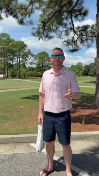 A golfer in a pink polo shirt standing beneath a pine tree beside the fairway at Gulf Shores Golf Club